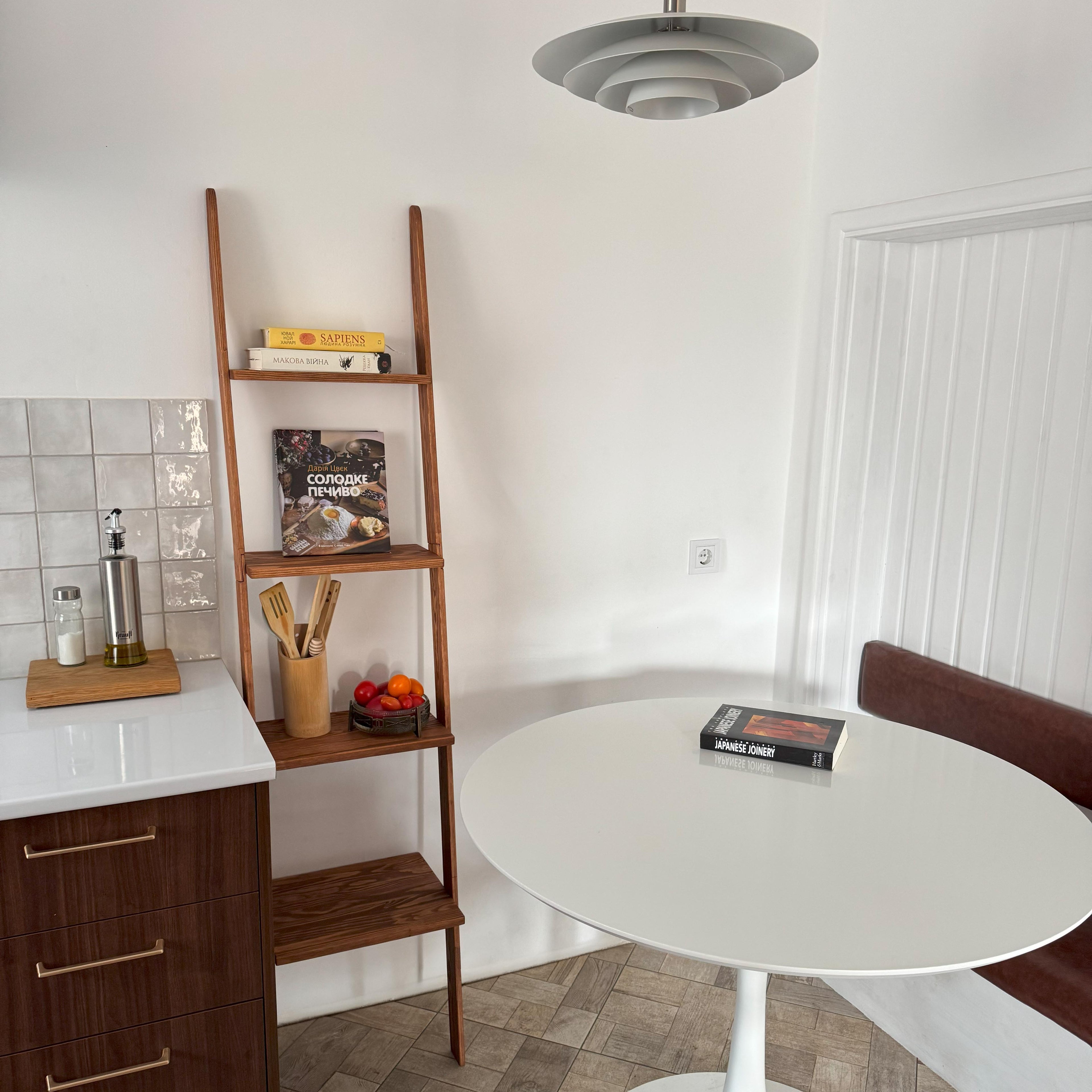 Small kitchen with a round white table, wooden shelf, and white walls.