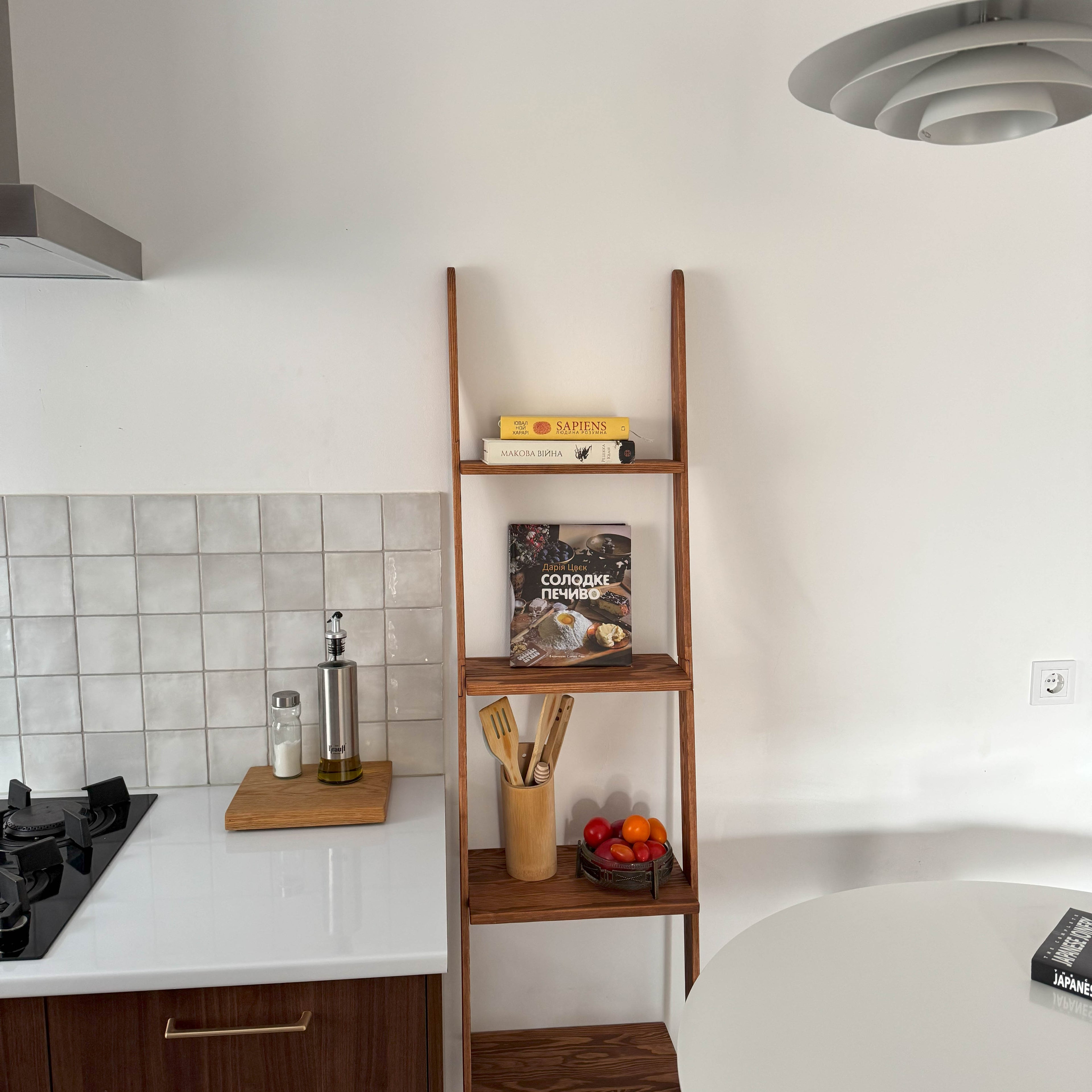 Wooden ladder shelf in a kitchen with cookbooks and a fruit bowl.